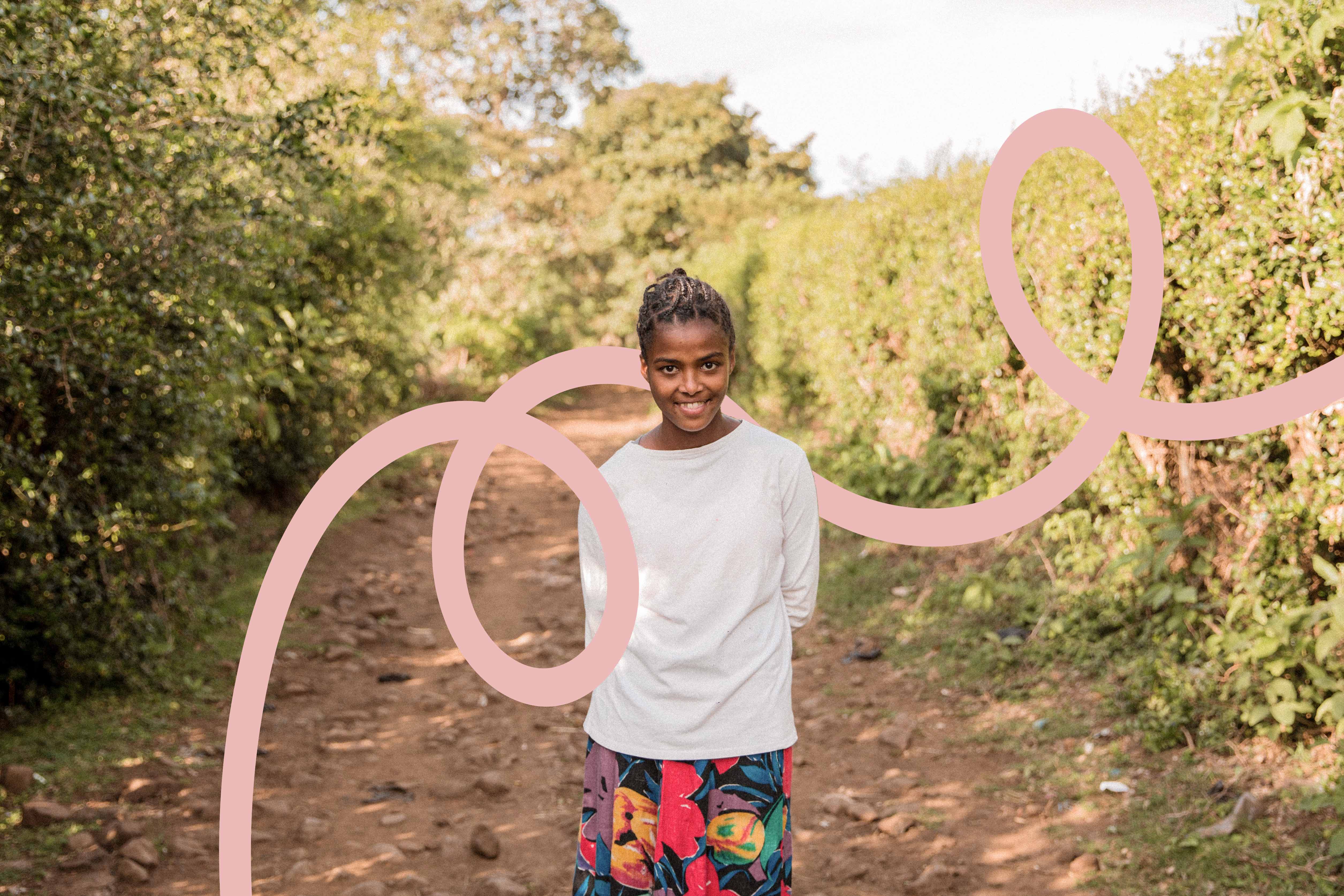 A smiling young person stands on a rocky dirt path lined with greenery. A pink, swirling line is digitally drawn over the image, looping around the person and across the path.