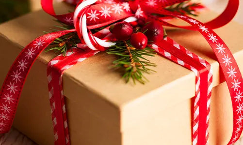 A brown gift box decorated with red ribbon, a candy cane, pine needles, and red berries, resting on a light wooden surface.