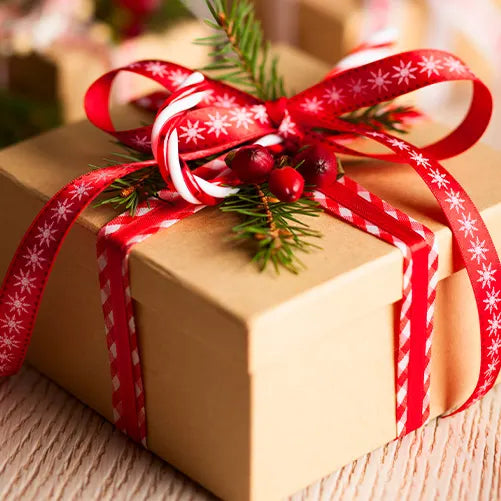 A brown gift box decorated with red ribbon, a candy cane, pine needles, and red berries, resting on a light wooden surface.