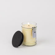 A lit 8oz Laundry Line Jar Candle by Bridgewater Candle Company sits in a clear glass jar with a black lid and tag, evoking fresh laundry scents against a plain white background.