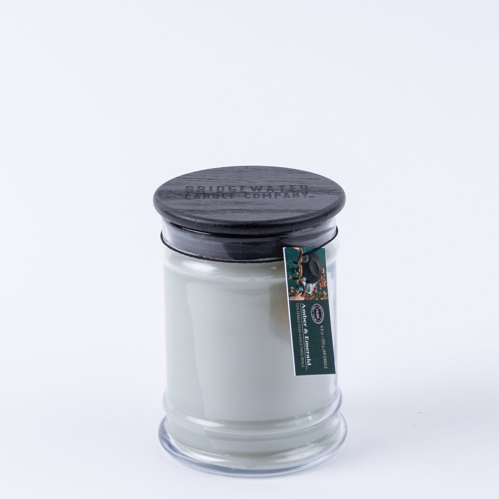 The Bridgewater Candle Company Amber & Emerald 8oz Jar Candle features soy-blend wax in a clear glass jar with a black lid and small tag, set against a plain white background.