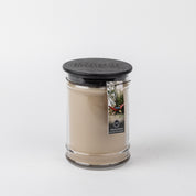 The Bridgewater Candle Company Afternoon Retreat 18oz Large Jar Candle features a beige fragrance in a clear glass jar with black lid and label with a person in a hammock. Enjoy its calming scent in any room. Background is plain white.