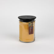 The Bridgewater Candle Autumn Gold Large Jar Candle features soy-blend wax in a glass jar with a black lid. A brown label with text and a small colorful image wraps around the jar’s neck, all set against a plain white background.