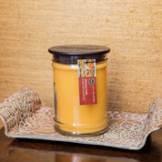 The Bridgewater Candle Autumn Gold Large Jar Candle, featuring orange soy-blend wax and a black lid, rests on a decorative tray. Its label displays Autumn Gold, set against a textured tan wall in the background.