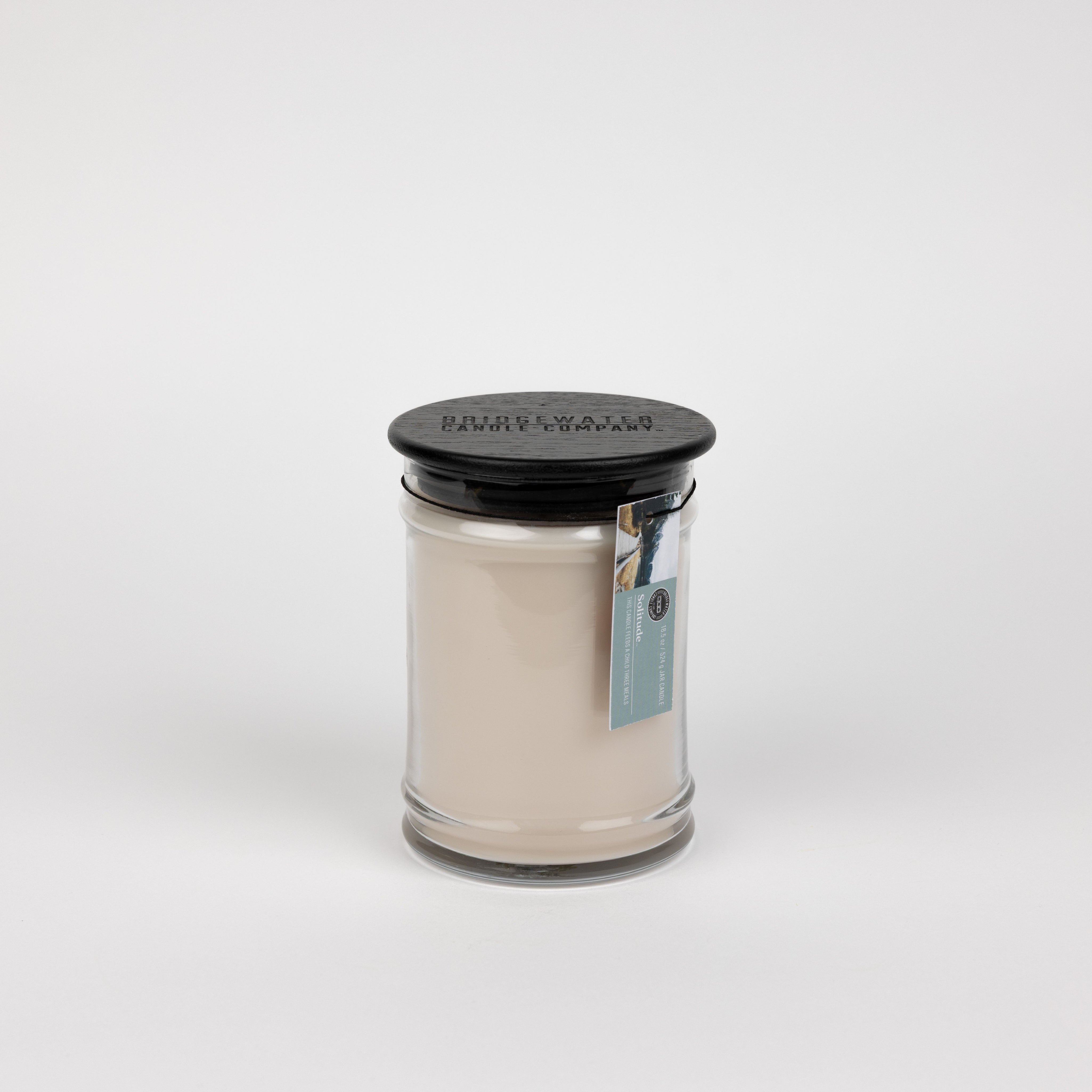 The Bridgewater Candle Solitude Large Jar Candle features soy-blend wax in a clear glass jar with a black lid and blue tag, displayed against a plain white background.