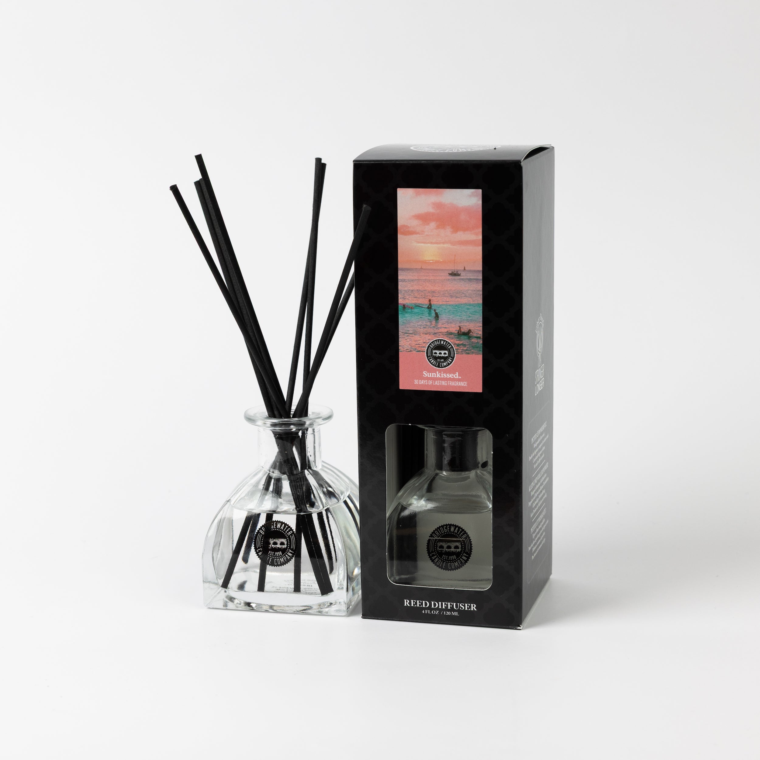 The Bridgewater Candle Sunkissed Reed Diffuser, featuring black reeds in a clear glass bottle and a beach sunset-themed black box, adds a stylish touch and fresh fragrance to your home décor.