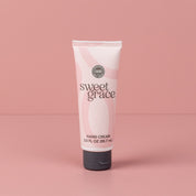 A pink and white tube of Bridgewater Candle Company Sweet Grace Hand Cream, 3.0 fl oz (88.7 ml) with a flip-top gray cap, stands upright on a pink surface against a matching background.