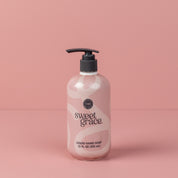 A bottle of Bridgewater Candle Companys Sweet Grace Liquid Soap with a pump dispenser and a pink and white abstract design sits against a matching pink background.