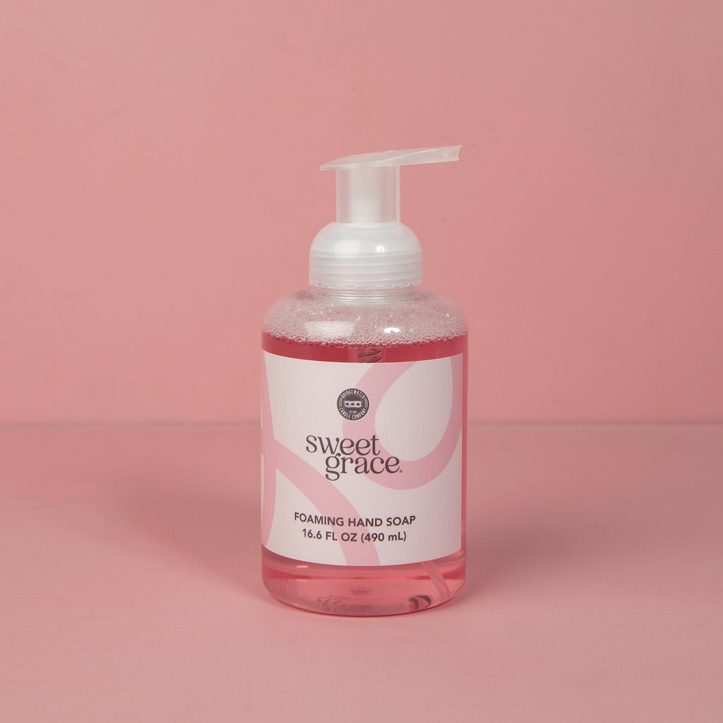 A clear plastic bottle of Bridgewater Candle Company’s Sweet Grace Foaming Hand Soap, 16.6 fl oz (490 ml), with an oriental scent and moisturizing aloe, sits on a pink surface with a white pump against a pink background.