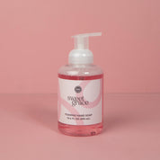 A clear plastic bottle of Bridgewater Candle Company’s Sweet Grace Foaming Hand Soap, 16.6 fl oz (490 ml), with an oriental scent and moisturizing aloe, sits on a pink surface with a white pump against a pink background.