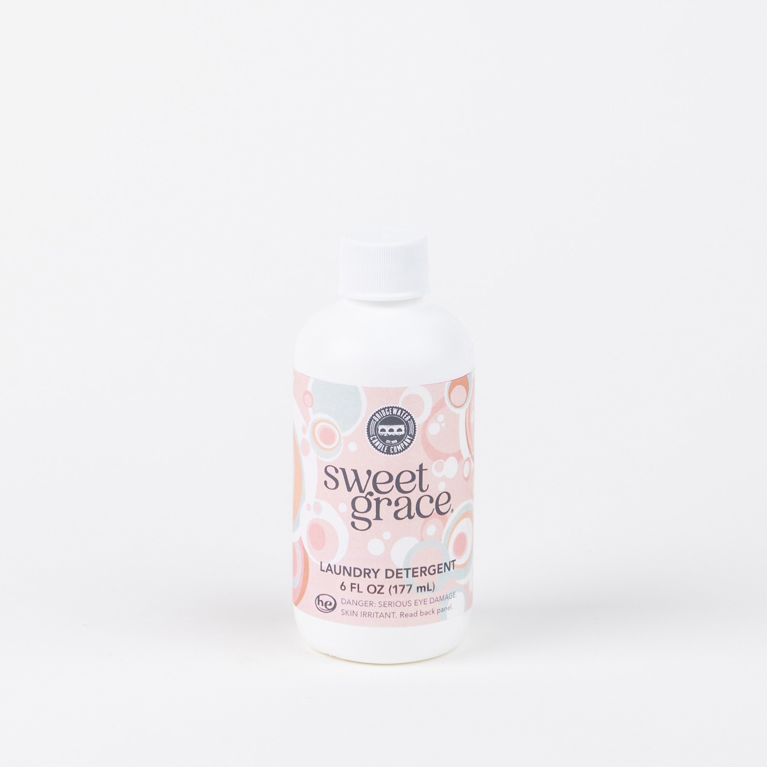 A 6oz bottle of Bridgewater Candle Companys Sweet Grace Laundry Detergent, with a pink and white circular label, stands upright against a plain white background. This fabric-safe detergent provides a long-lasting scent.