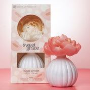 A pink and white Sweet Grace Flower Diffuser by Bridgewater Candle Company, shaped like a round vase with delicate petals, is displayed next to its packaging labeled "Fragrance: Sweet Grace Flower Diffuser 8 fl oz (236 mL).