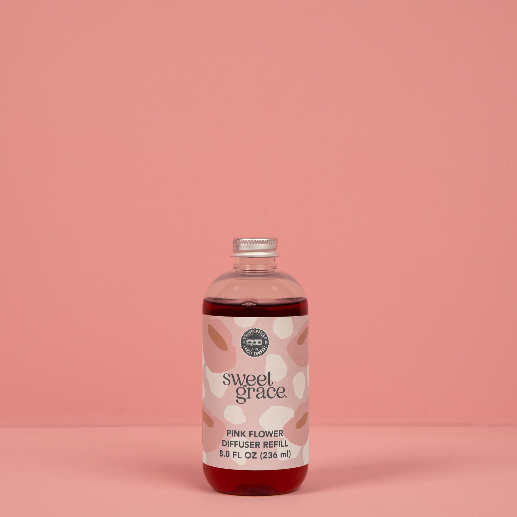 A clear plastic bottle of Sweet Grace Flower Diffuser & Refill Bundle by Fast Bundle, filled with pink liquid, makes a perfect fragrance gift and is shown against a solid pink background.