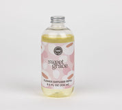 A clear bottle with a silver cap, filled with yellow liquid and labeled Bridgewater Candle Sweet Grace Dye-Free Flower Refill. The long-lasting fragrance refill has a pink label with white abstract patterns and sits on a plain white background.