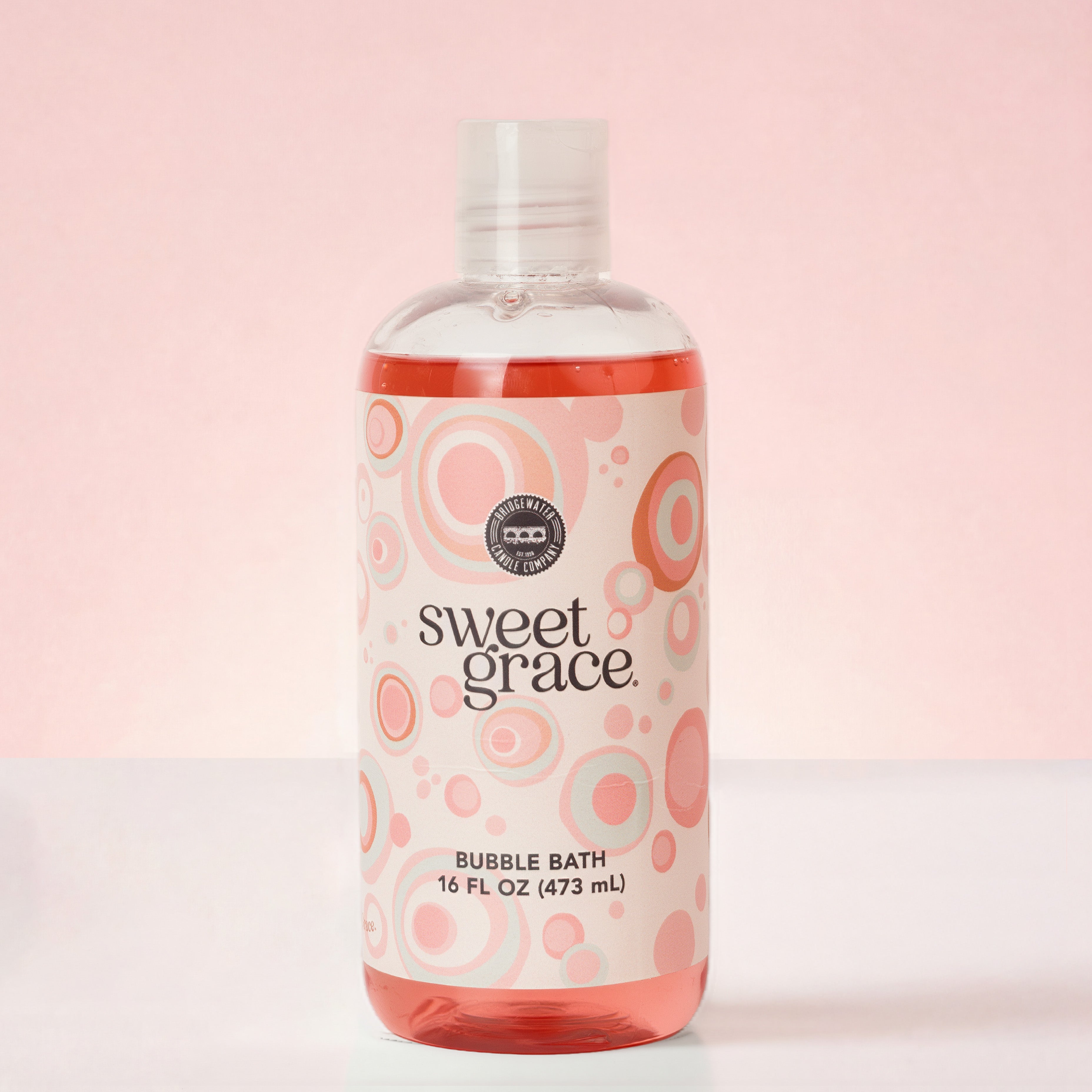 A clear 16 FL OZ (473 mL) bottle of Bridgewater Candle Sweet Grace Bubble Bath with a label featuring pink and grey concentric circles.