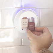 A hand inserts a Pura+Bridgewater Fragrance Refill - Welcome Home by Bridgewater Candle Company into a white smart home diffuser plugged into a tiled wall outlet.