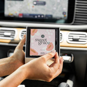 Someone holds a boxed Bridgewater + Pura Car Diffuser Cartridge Sweet Grace by Bridgewater Candle Company inside a car, with the dashboard and navigation screen visible in the background.