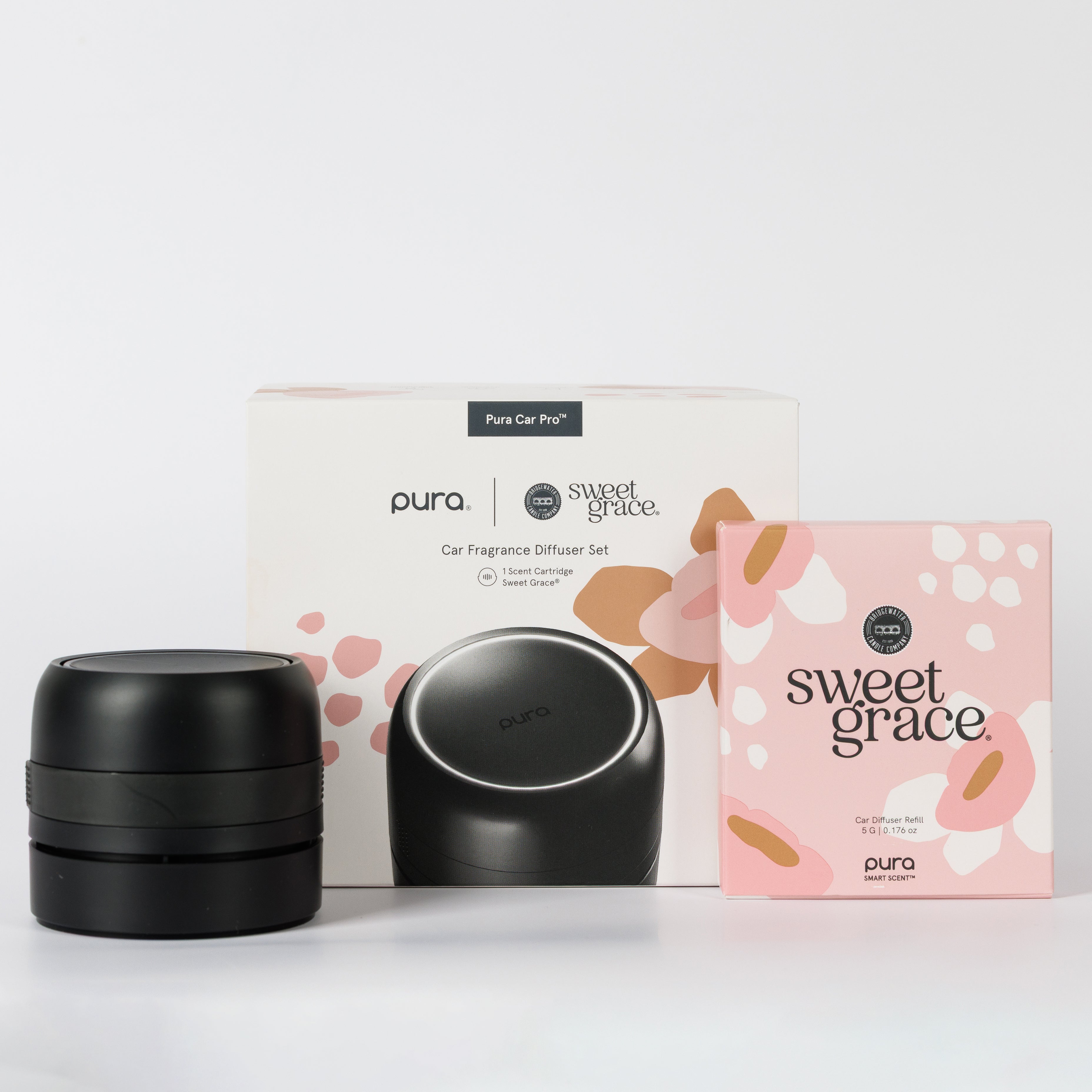 A Bridgewater + PURA Sweet Grace Car PRO Diffuser Set by Bridgewater Candle is shown with the black diffuser in front of its white branded box, next to a pink Sweet Grace refill box, offering a long-lasting car fragrance experience.