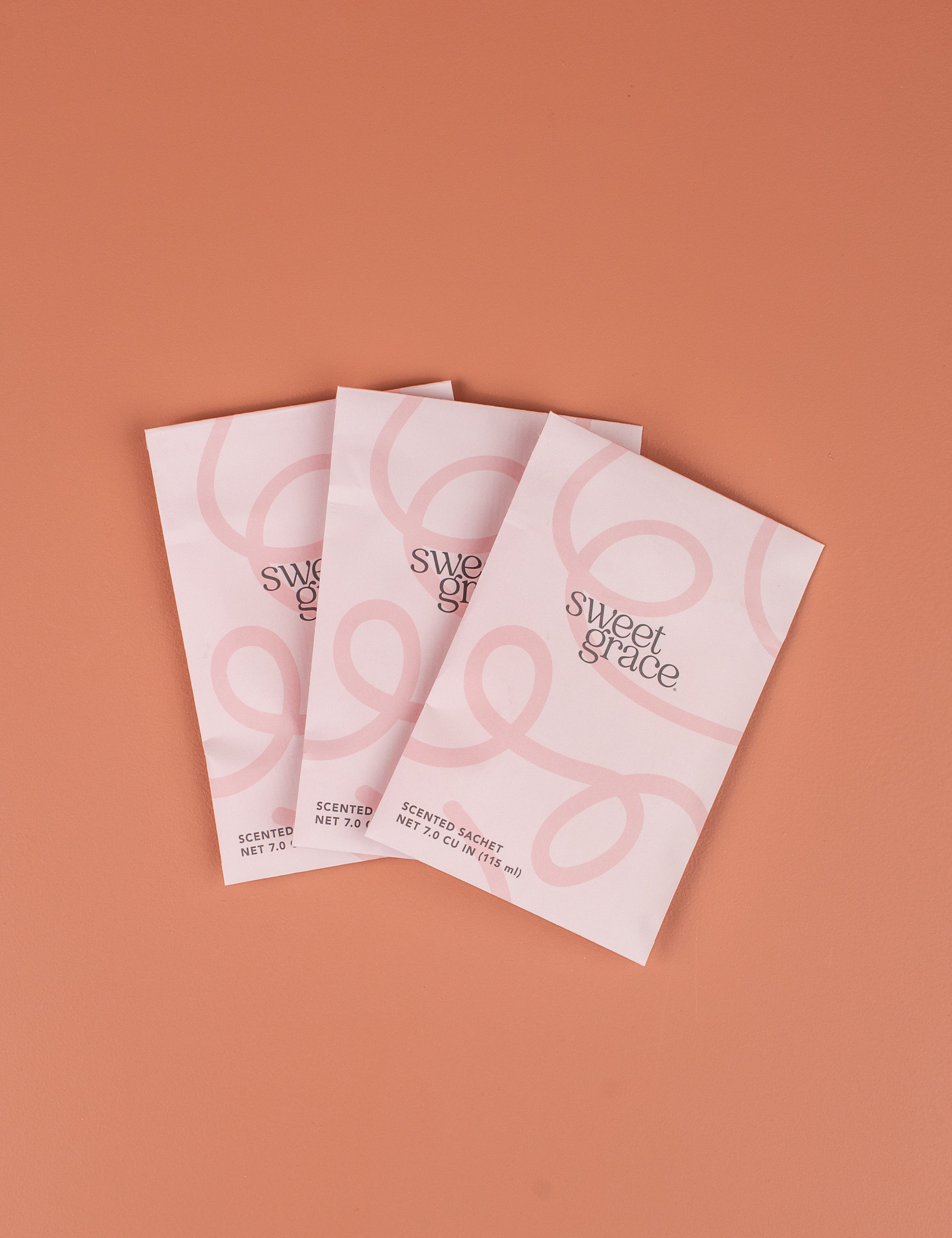 Three Bridgewater Candle Company Sweet Grace Modern Swirl Sachets are arranged in a fan shape on a soft pink background, offering an elegant way to fragrance any room.