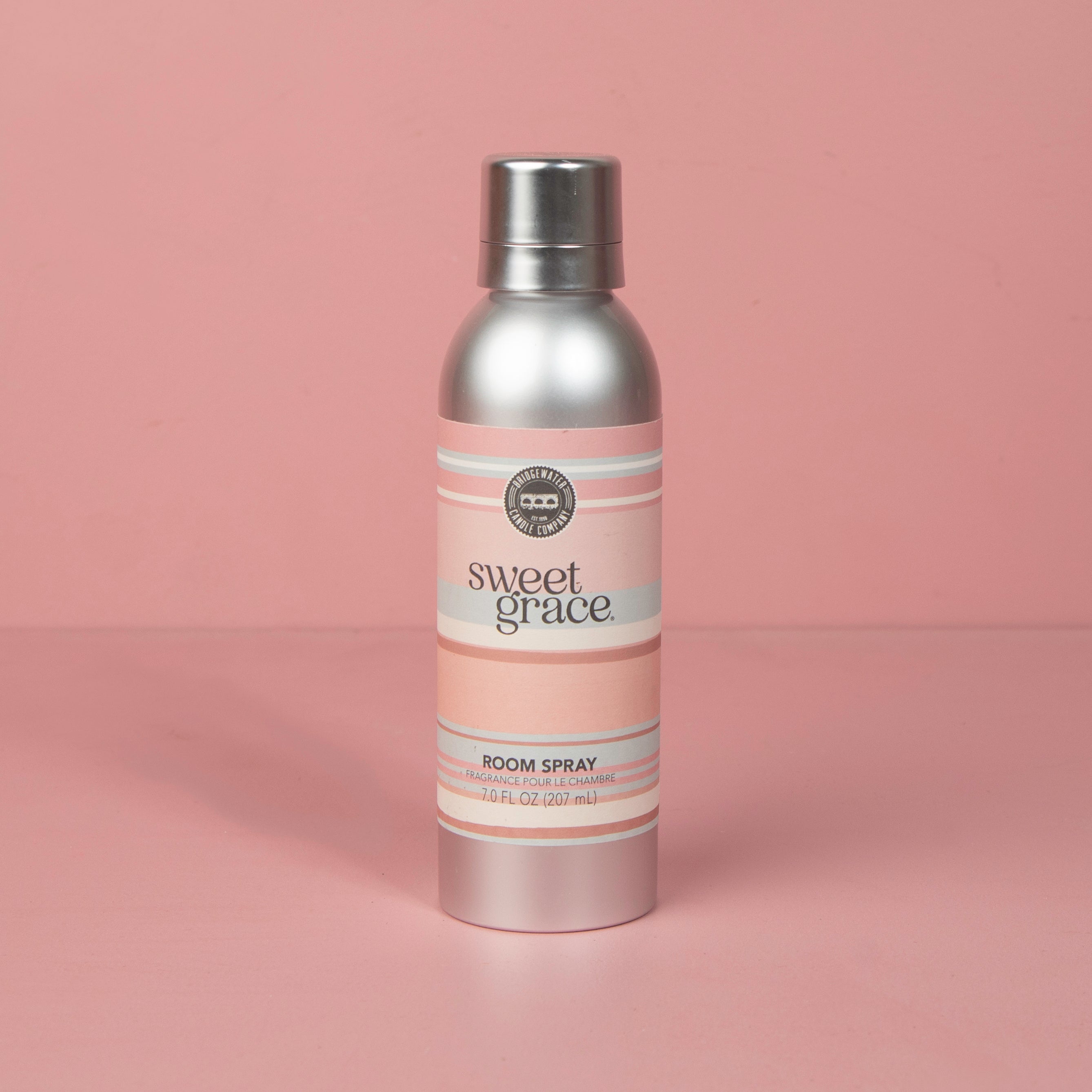 A silver can of Bridgewater Candle Company’s Sweet Grace Non-Aerosol Room Spray with a pink label stands upright against a plain pink background, bringing stylish elegance to your home fragrance routine.