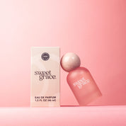A frosted pink bottle of Sweet Grace Eau de Parfum with a glossy pink ball top, displayed next to its packaging box on a pink background.