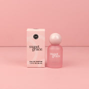 A Sweet Grace Eau de parfum box and frosted pink Sweet Grace eau de parfum bottle with pink round ball cap on pink background