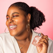 A woman smiling while holding a bottle of Sweet Grace perfume