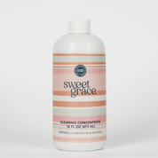 A 16 fl oz (473 mL) bottle of Bridgewater Candle's Sweet Grace Cleaning Concentrate | Mop Soap, featuring pink, cream, and gray stripes with a white cap, is displayed against a plain white background. This stylish and fragrant cleaner combines an appealing design with effective cleaning for your home.