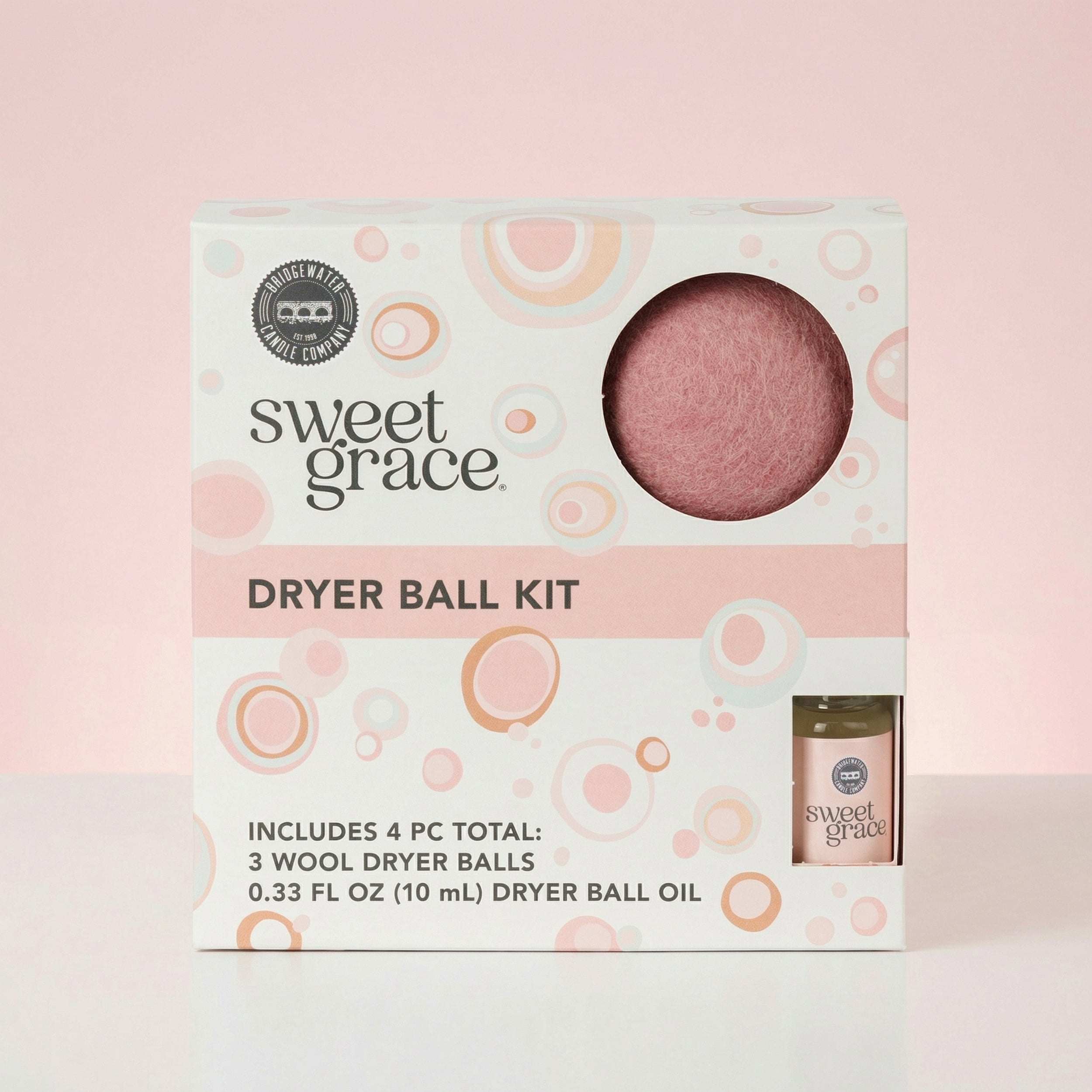 A Sweet Grace Dryer Ball Kit box with circular patterns contains 3 pink wool dryer balls and a 10 mL bottle of dryer ball oil.