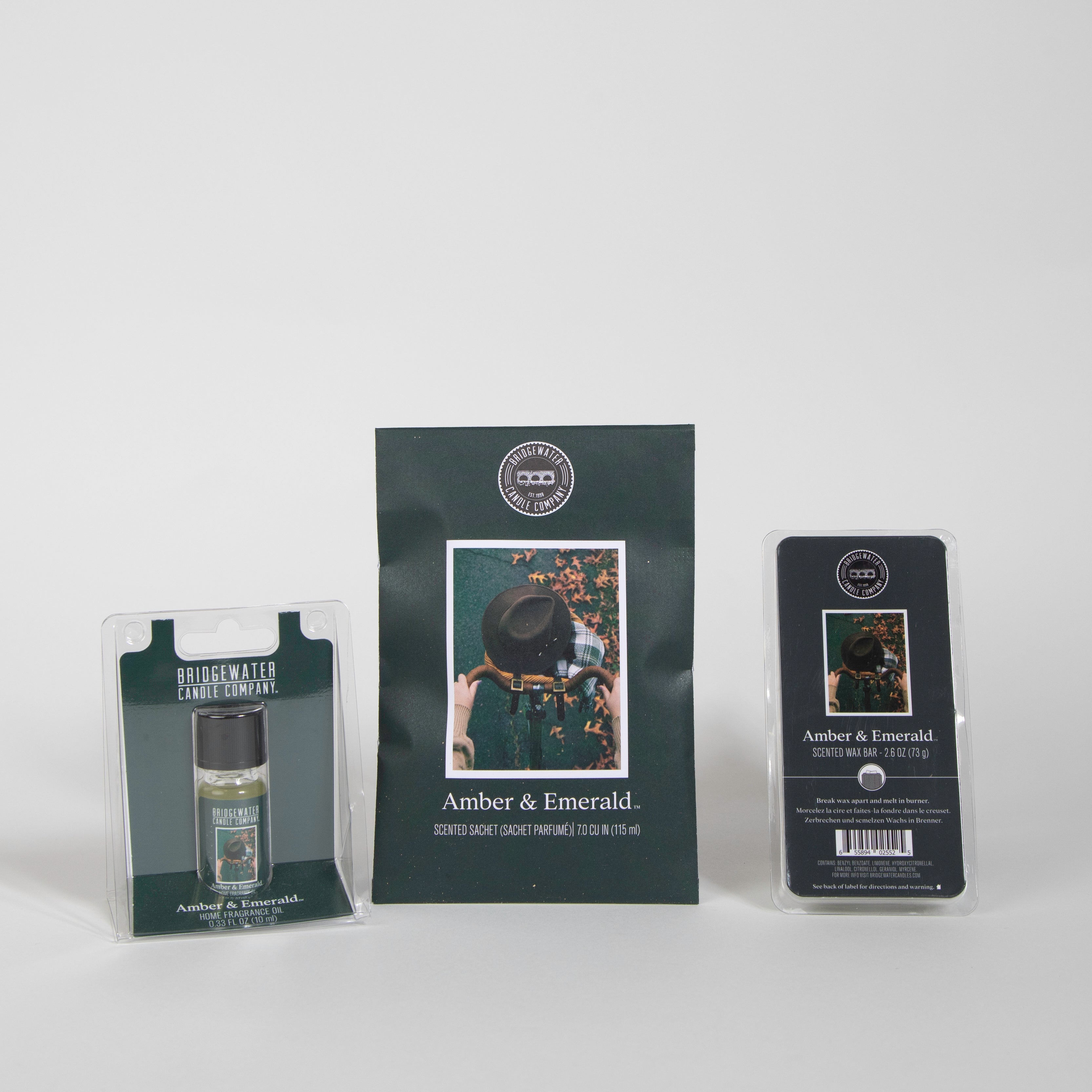 Bridgewater Candle Companys Amber & Emerald Flameless Bundle—featuring a scented sachet, home fragrance oil bottle, and wax bar with dark green labels—is displayed against a white background.
