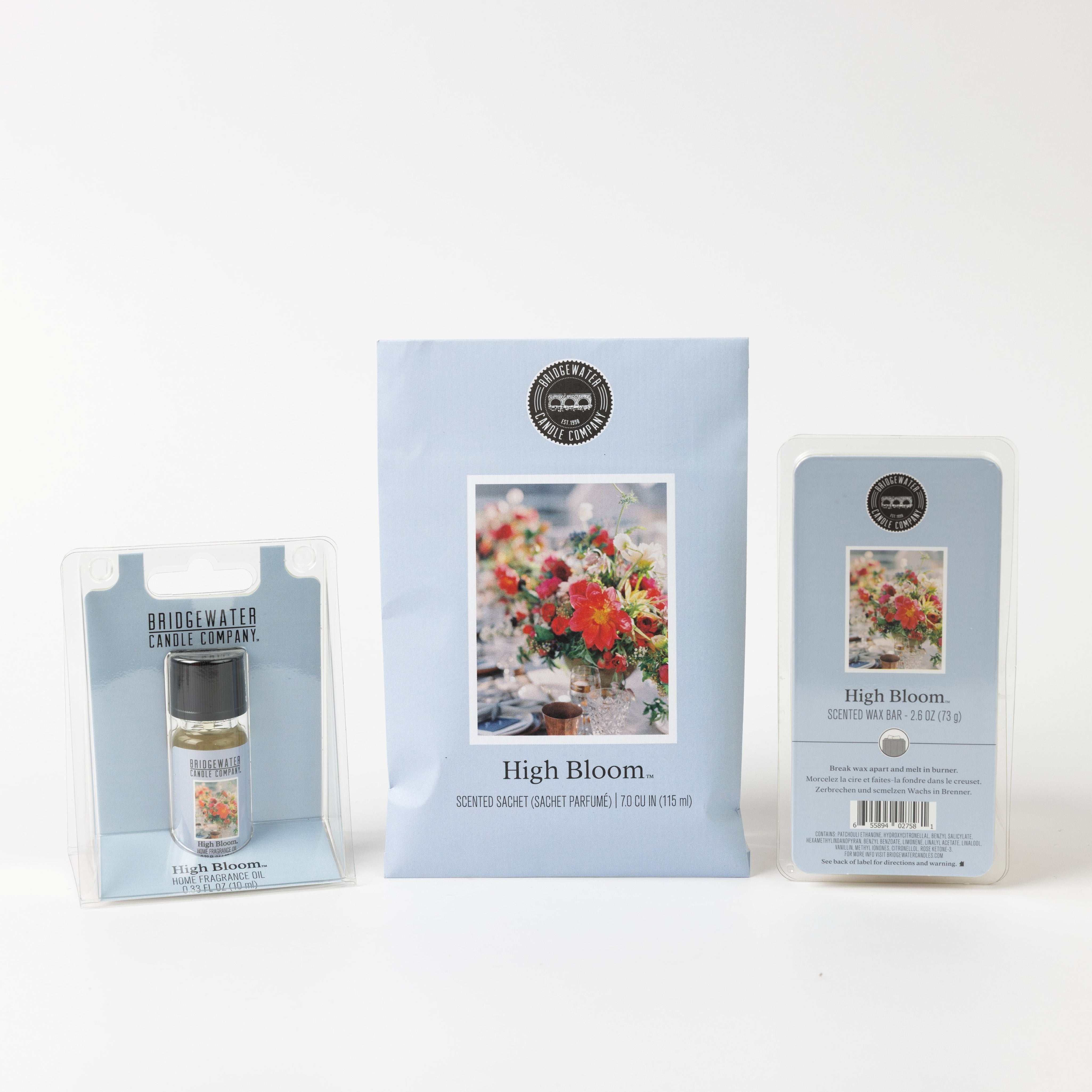 Bridgewater Candle's High Bloom Flameless Bundle, including an air freshener spray, scented sachet, and wax melt with floral label designs, is displayed against a white background adorned with vibrant flower arrangements.
