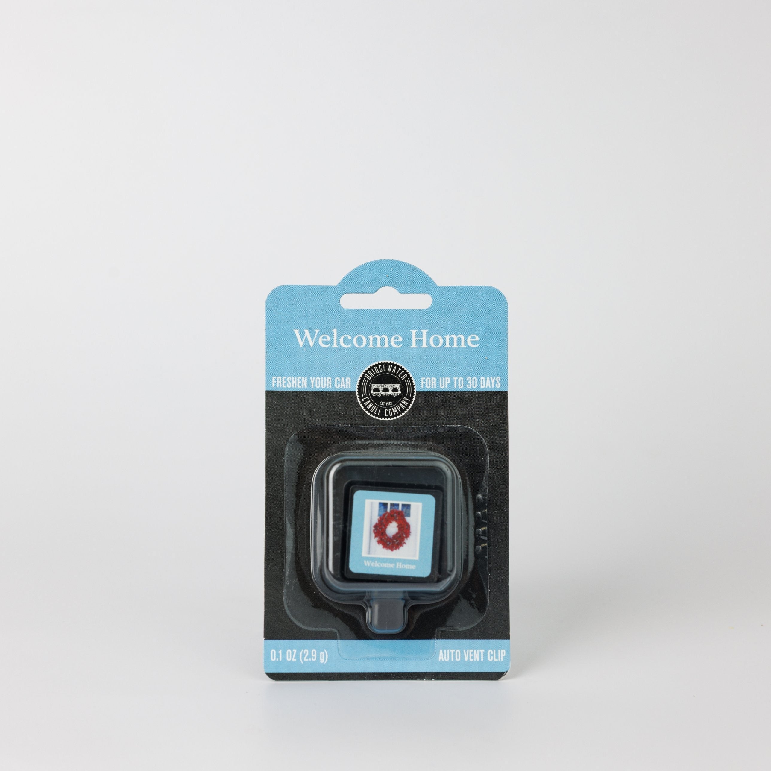 A square Bridgewater Candle Auto Vent Clip-Welcome Home in a blue and black hanging retail package featuring a picture of a wreath on a door.