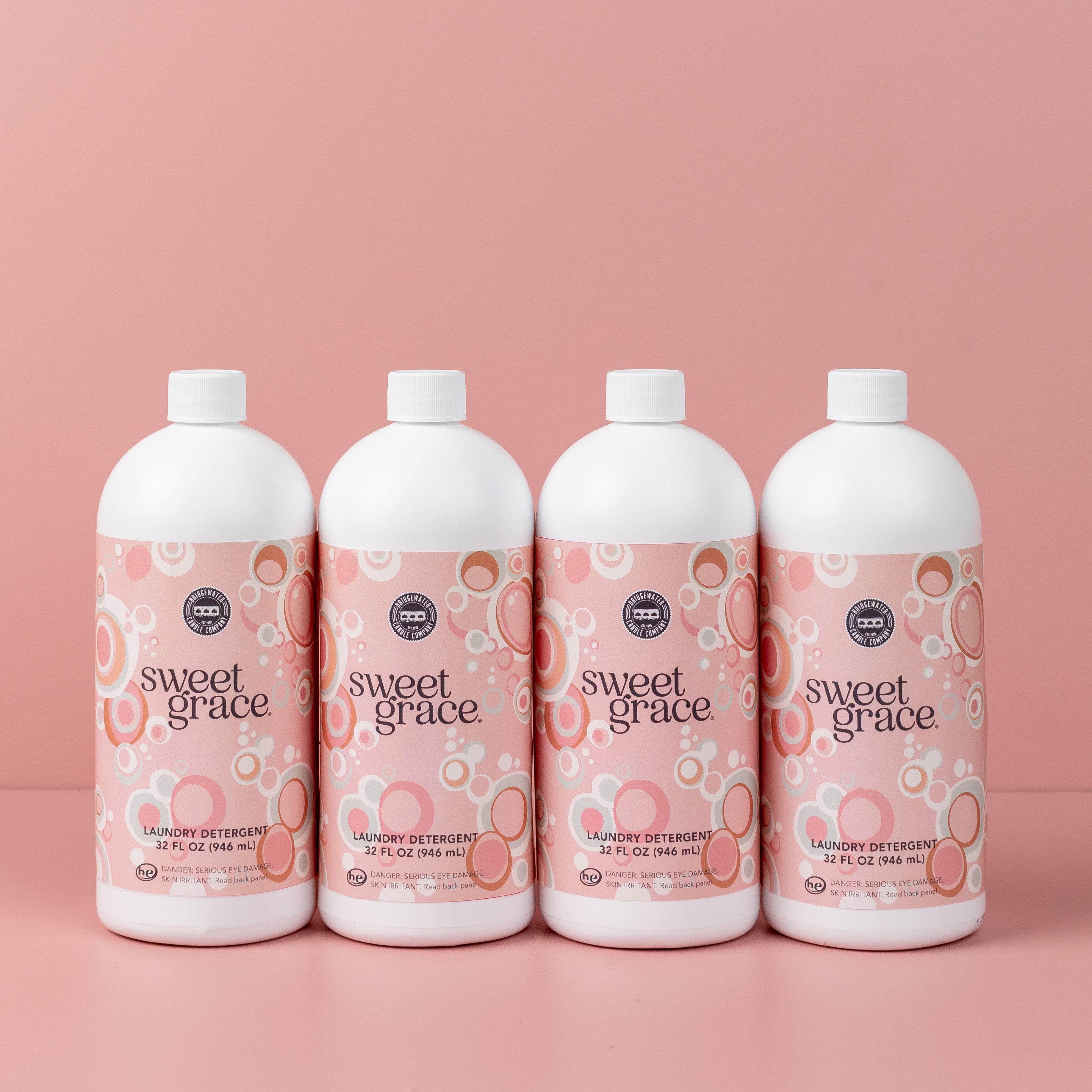 Four bottles from the Fast Bundle Back to School Laundry Bundle 4pk, each featuring pink and orange bubble designs on the label, are lined up in front of a plain pink background—perfect for those who love fresh-smelling laundry with a touch of elegance.