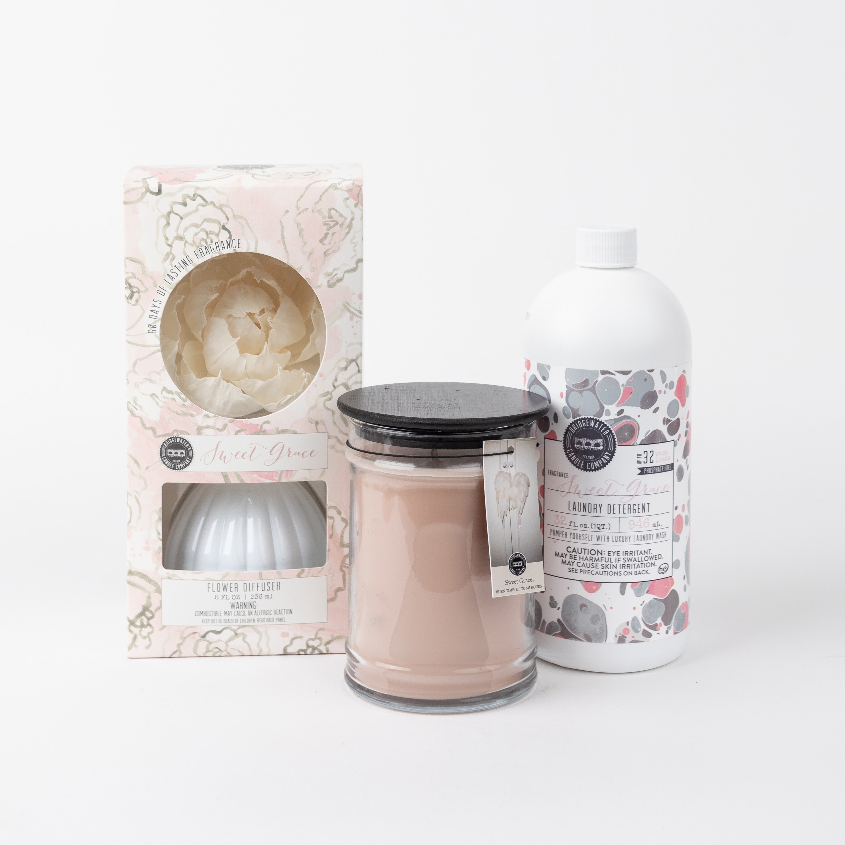Three home fragrance products: a boxed flower diffuser, a large scented candle in a glass jar with a black lid, and a white bottle of laundry detergent with a patterned label, all displayed on a white background.