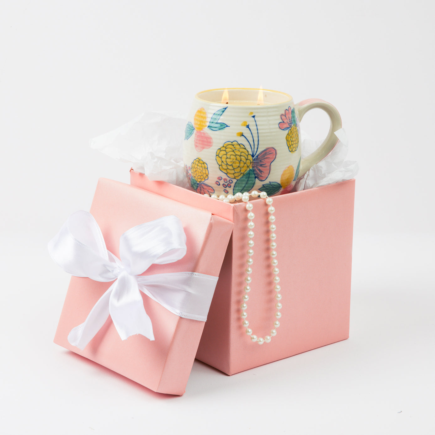 A Bridgewater Candle Sweet Grace Mug Candle and a pearl necklace are arranged in an open pink gift box with a white ribbon, set against a plain white background.