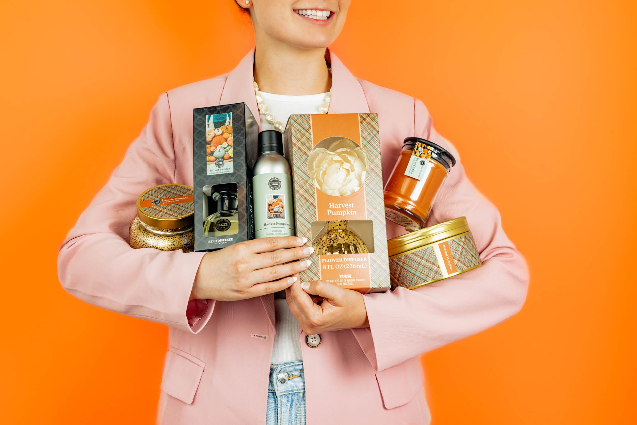 Person holding various Harvest Pumpkin products against an orange background