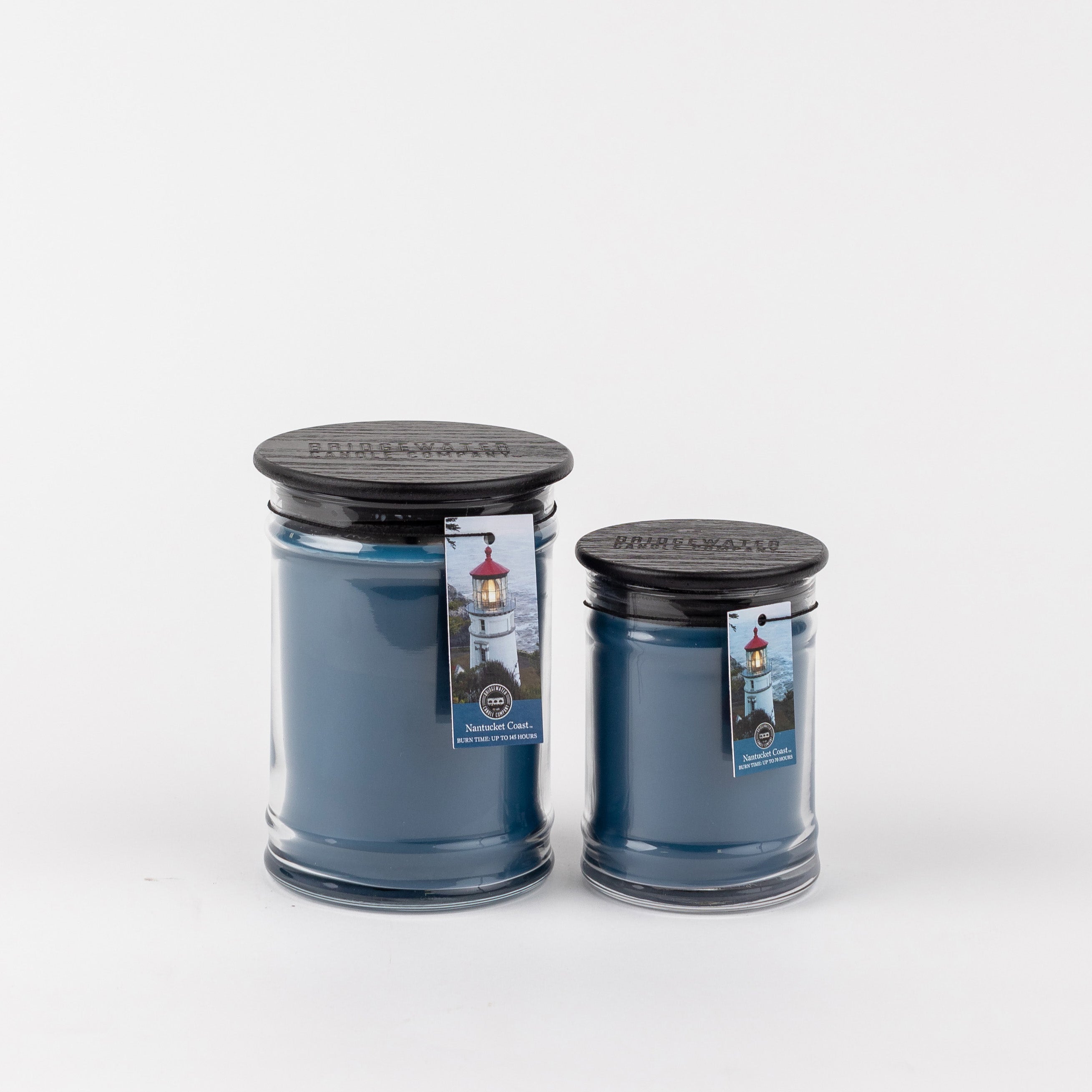 Two Nantucket Coast 8oz Jar Candles by Bridgewater Candle Company, each with blue wax, black wooden lids, and a lighthouse tag, are displayed side by side on a white background for coastal-inspired charm.