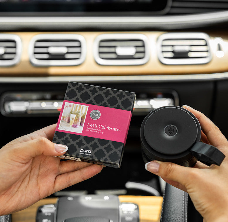 Person holding a let's celebrate car diffuser and its packaging inside a car's interior.