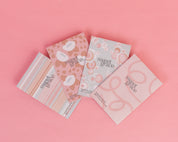 Four Bridgewater Candle Company Sweet Grace Modern Stripe Sachets are arranged in a fan shape on a pink background, featuring pastel colors and striped designs—perfect for enhancing any space with a fresh home fragrance.