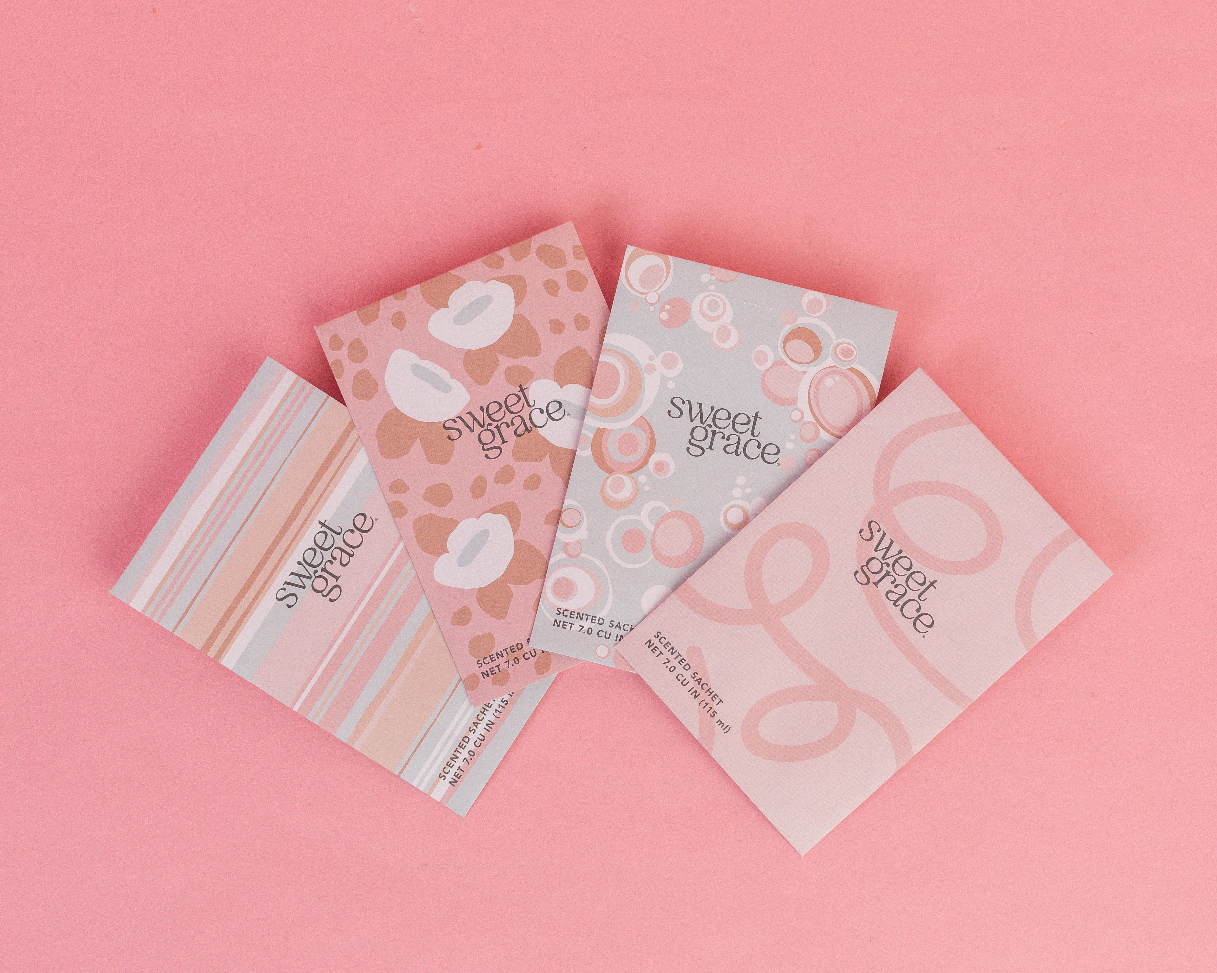 Four Bridgewater Candle Company Sweet Grace Modern Stripe Sachets are arranged in a fan shape on a pink background, featuring pastel colors and striped designs—perfect for enhancing any space with a fresh home fragrance.