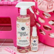 The Fast Bundle Sweet Grace Stain Remover Bundle features a large spray bottle and a small travel-size bottle, both displayed on pink tiles with laundry baskets and towels in the background.