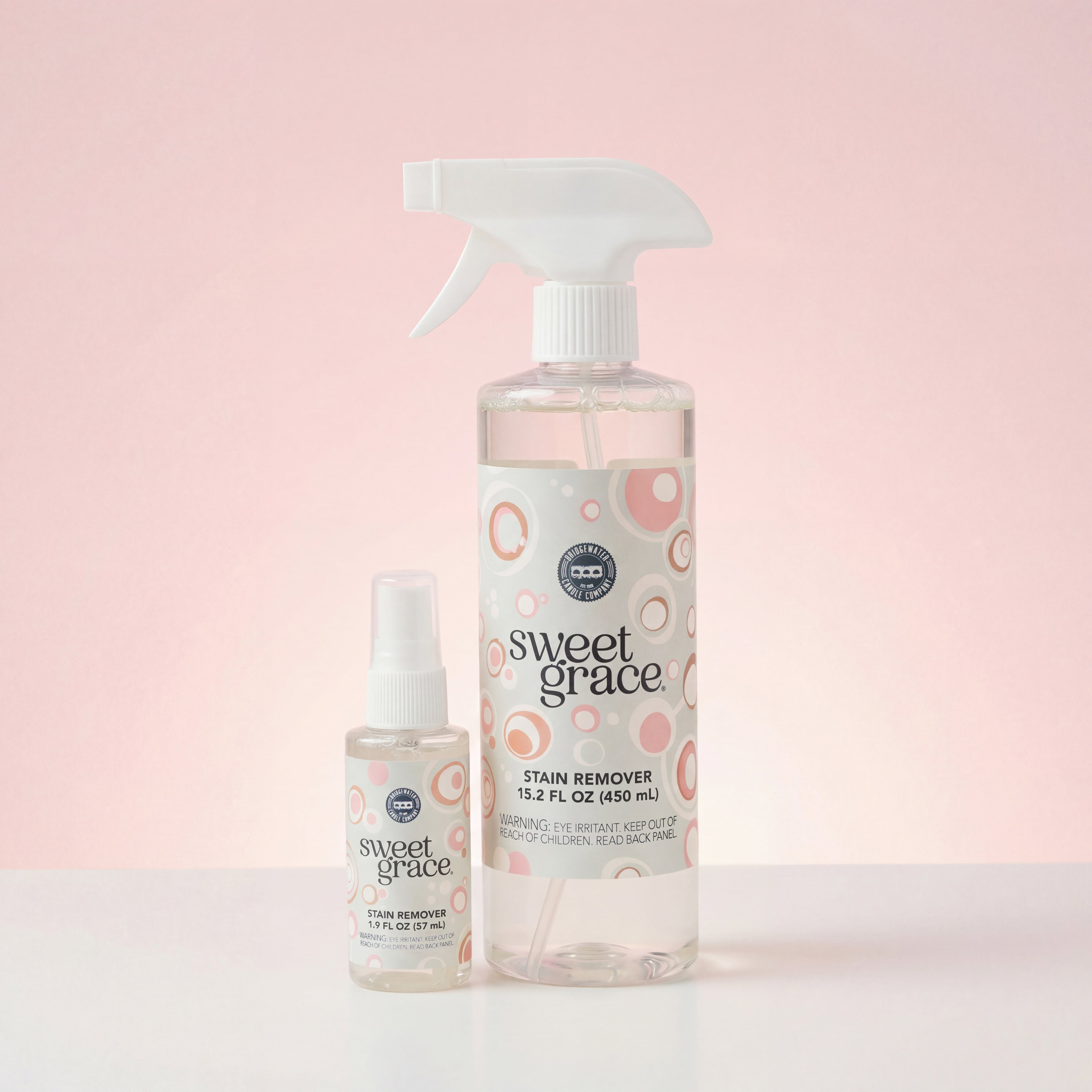 The Sweet Grace Stain Remover Bundle by Fast Bundle includes one large spray bottle and one small bottle, both with white labels featuring pink and beige circular designs, displayed against a pale pink background.