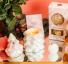 The Bridgewater Candle Sweet Grace Collection Candle #70 in a white ceramic holder sits on a table with festive décor, creating a charming holiday centerpiece.