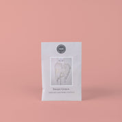 A Sweet Grace Sachet by Bridgewater Candle Company, adorned with angel wings and a delicate label, stands upright against a pink background—adding a charming touch of home fragrance.