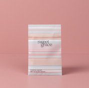 The Bridgewater Candle Company Sweet Grace Modern Stripe Sachet, infused with the signature Sweet Grace scent, stands upright on a pink surface and background. The sachet features pink and peach stripes with the product name displayed on the front.