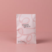 A light pink Sweet Grace Modern Swirl Sachet by Bridgewater Candle Company stands upright against a pink background, featuring a soft swirl design and elegant text—perfect for adding home fragrance.