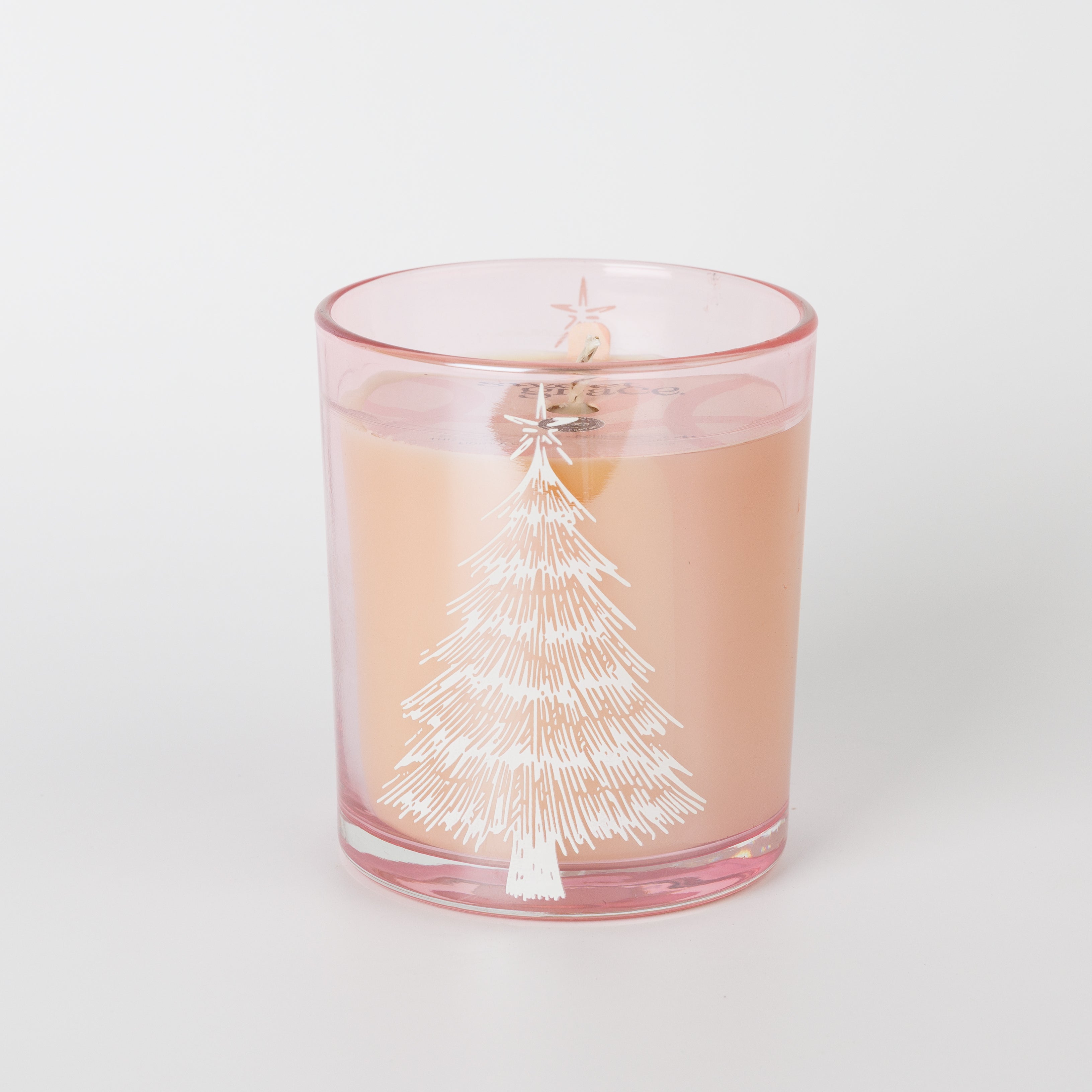 The Bridgewater Candle Sweet Grace Pink Tree Decal Jar Candle features a festive pink glass holder adorned with a white Christmas tree design and is filled with light peach-colored soy-blend wax. The visible wick and plain white background make this candle a charming holiday accent.