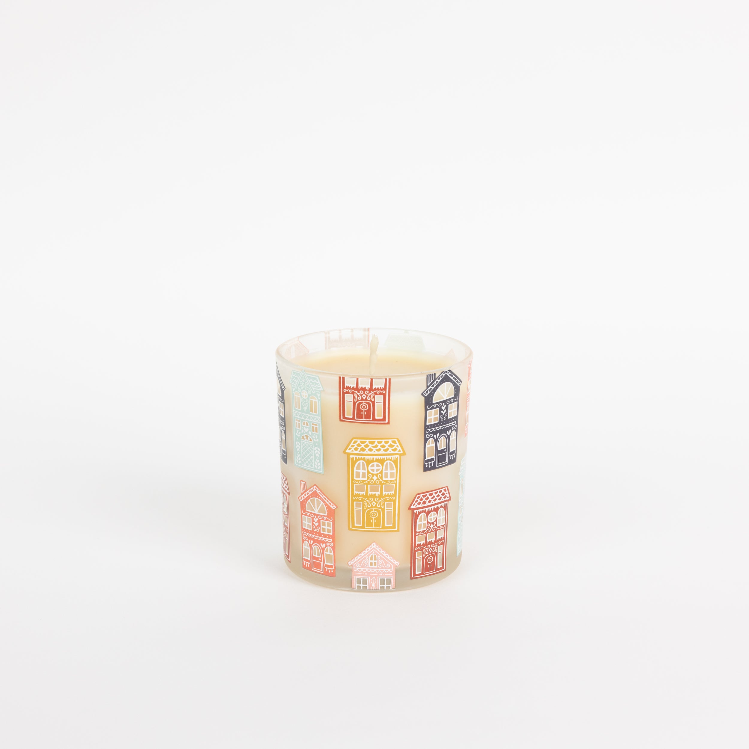 The Bridgewater Candle Sweet Grace Holiday House Candle features white soy-blend wax in a glass holder adorned with colorful house illustrations, all set against a plain white background.