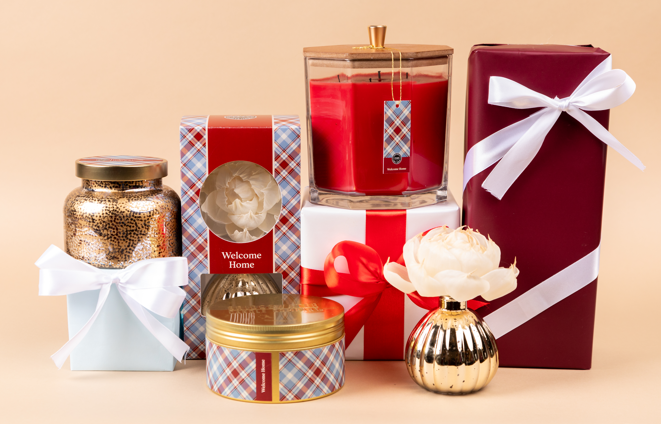 The Bridgewater Candle Company’s Welcome Home Large Decorative Candle features a soy-blend wax in an elegant gold jar, paired with wrapped gift boxes, a plaid tin, and floral accents—perfect for stunning home decor.