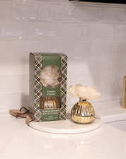 The Bridgewater Candle Company Festive Frasier Holiday Mercury Flower Diffuser in a gold vase sits on a white tray beside its green plaid box, bringing elegant holiday decor to the white kitchen countertop.